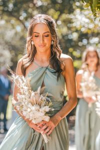 Bridesmaids and groomsmen laughing and posing with Zoe and Deon on the grass by the ocean at their Noosa wedding