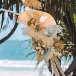 Luxe white circle arbour with neutral-colored dried florals against the ocean backdrop at Zoe and Deon’s Noosa wedding.