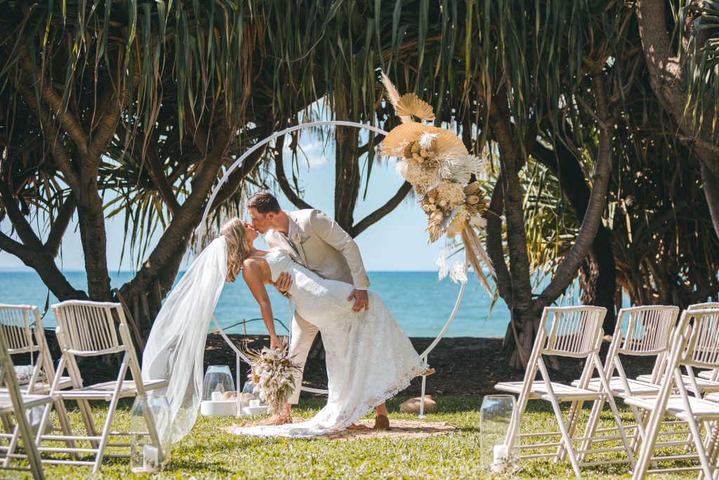 Zoe and Deon exchanging vows under the luxe white circle arbour with dried neutral florals at Maison La Plage, Noosa