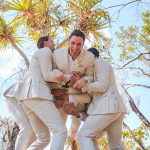 Bridesmaids and groomsmen laughing and posing with Zoe and Deon on the grass by the ocean at their Noosa wedding.