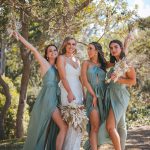 Bridesmaids and groomsmen laughing and posing with Zoe and Deon on the grass by the ocean at their Noosa wedding.