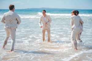 Bridesmaids and groomsmen laughing and posing with Zoe and Deon on the grass by the ocean at their Noosa wedding.