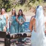 Bridesmaids and groomsmen laughing and posing with Zoe and Deon on the grass by the ocean at their Noosa wedding.