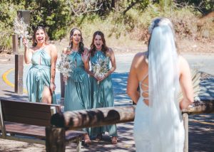 Bridesmaids and groomsmen laughing and posing with Zoe and Deon on the grass by the ocean at their Noosa wedding.